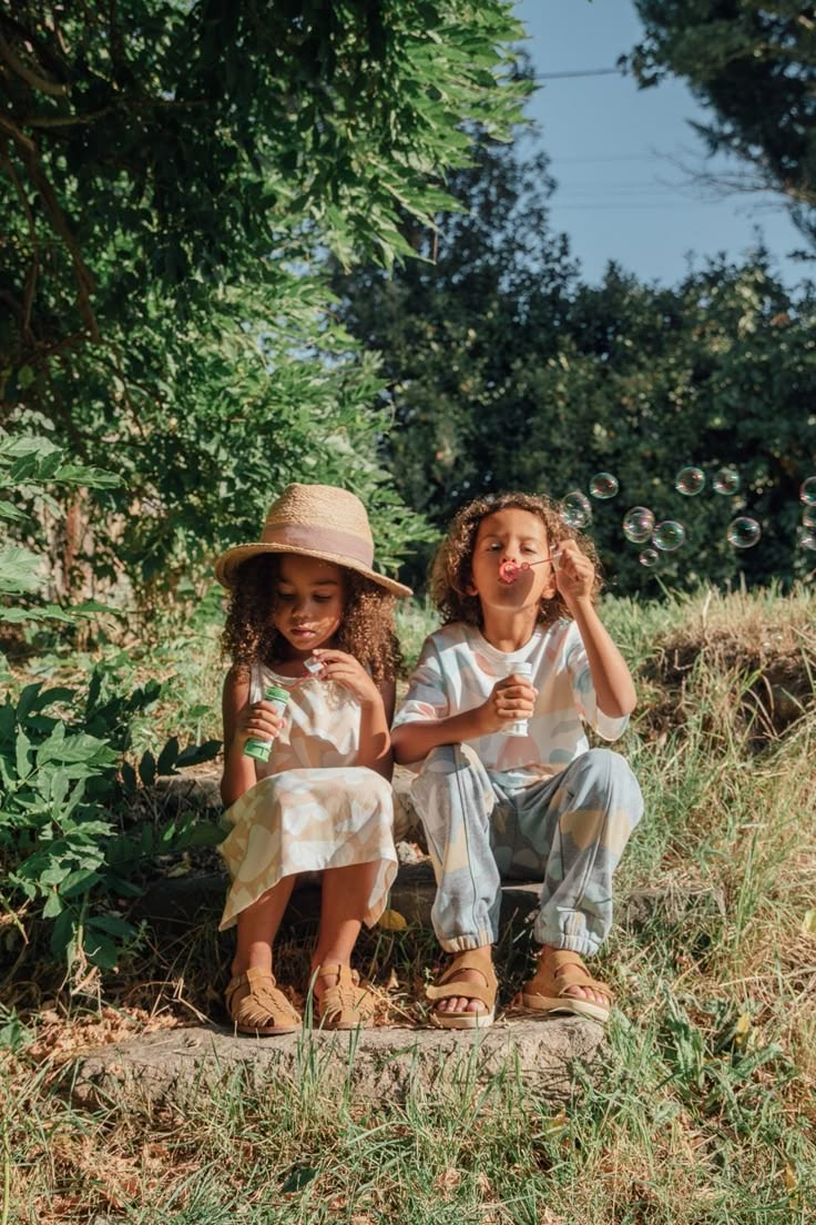 Two children blowing bubbles on a stone step in tall grass